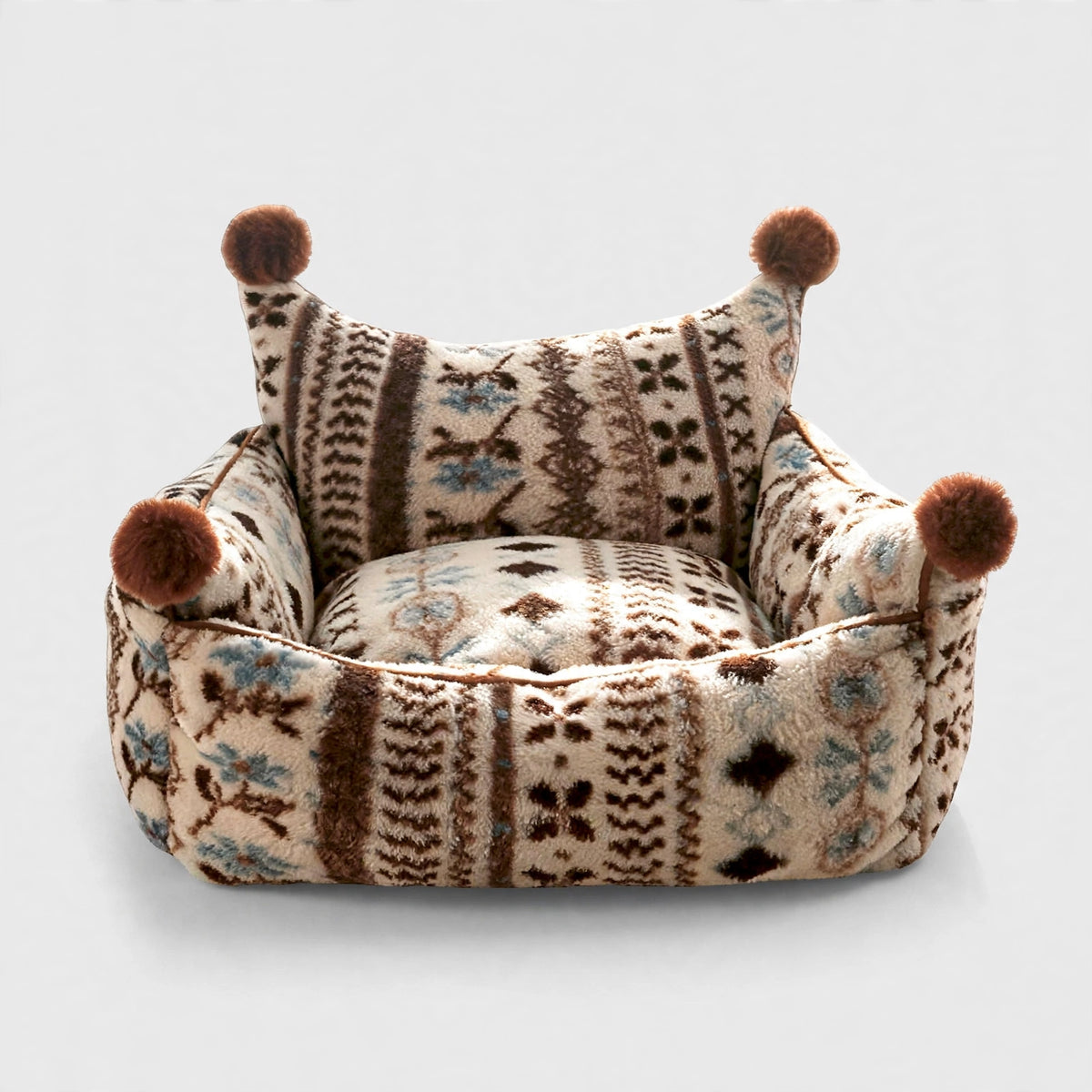 Patterned bolster pet bed with pom-pom corners on light background