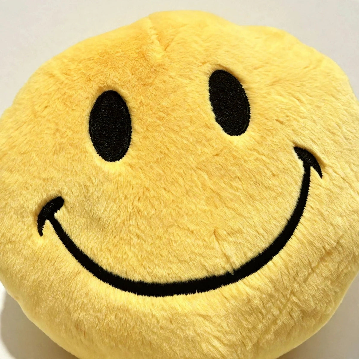 Close-up of yellow smiley face plush pillow texture and smile stitching